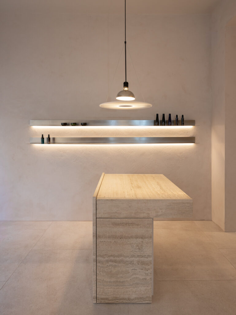 Travertine counter under a backlit stainless steel shelf at circlé salon, Bratislava